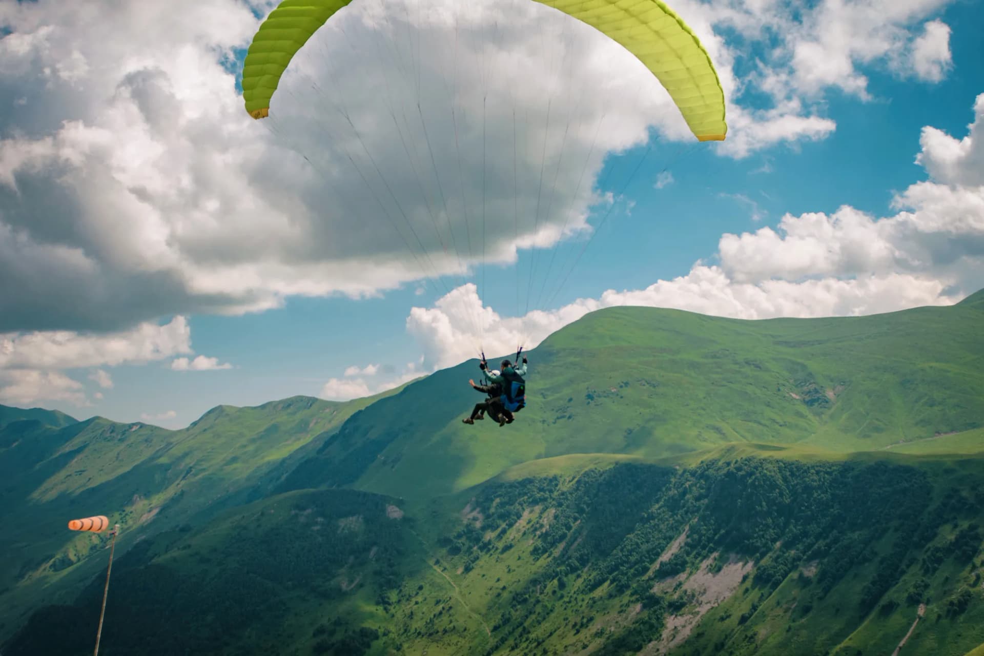 Tandem paraglider under a lime-green wing against a bank of summer cloud