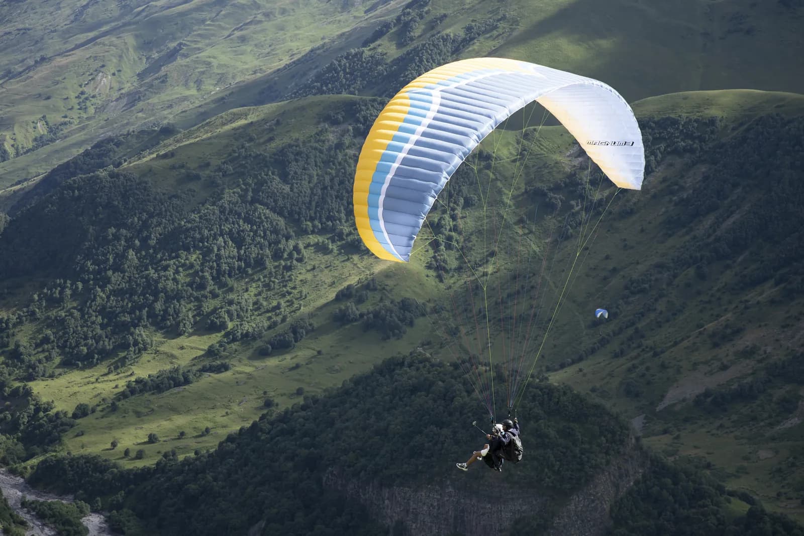 Tandem paraglider over the green Gudauri valley with the Caucasus ridge behind