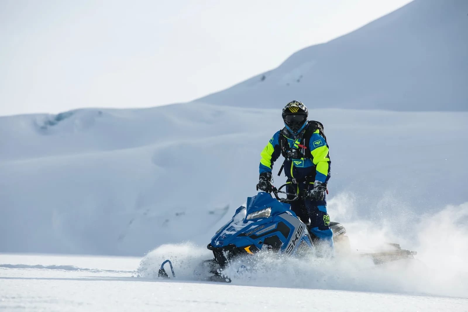 Snowmobile kicking up a wall of snow on the open slope