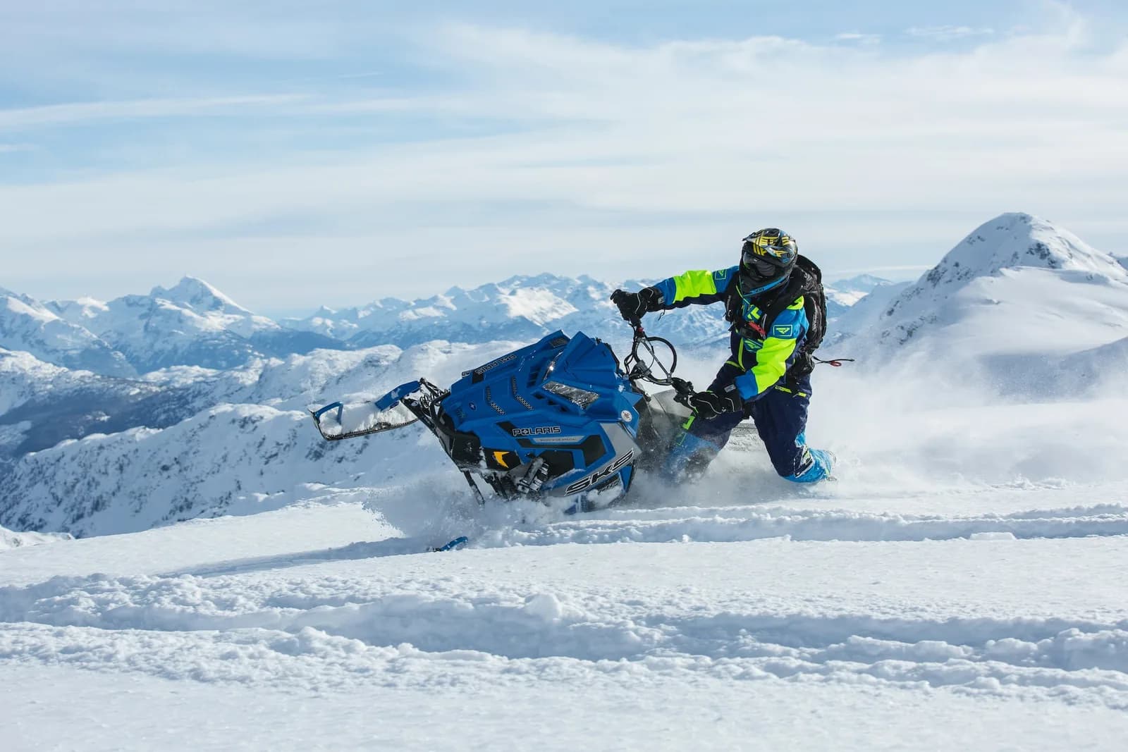 Rider leaning a snowmobile into a turn, spray flying, Caucasus peaks behind